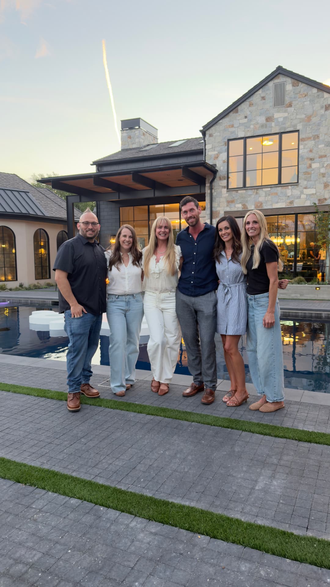 Lindy and a builder team outside a stone custom home at dusk